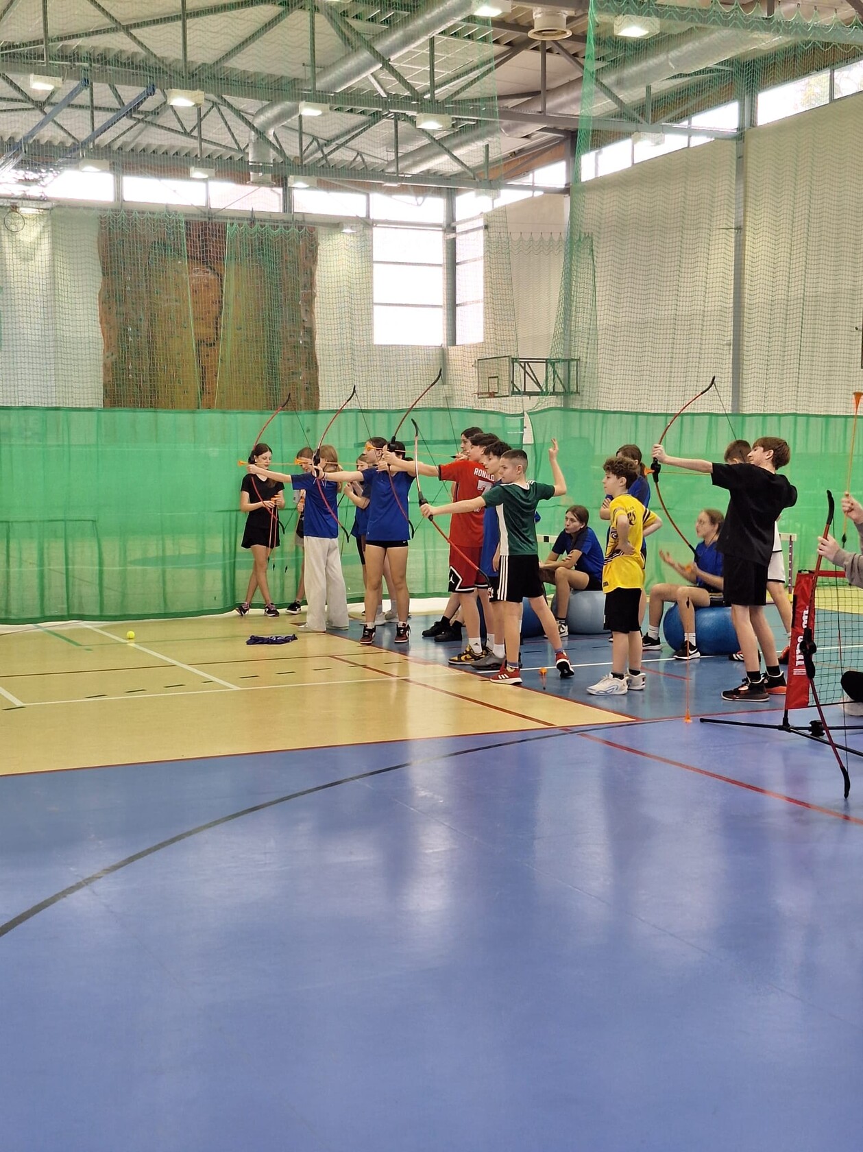 Uczestnicy półkolonii na sali gimnastycznej strzelają z łuku.